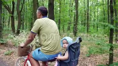 一个男人带着一个孩子在森林里骑自行车，夏天，孩子坐在一张特殊的椅子上